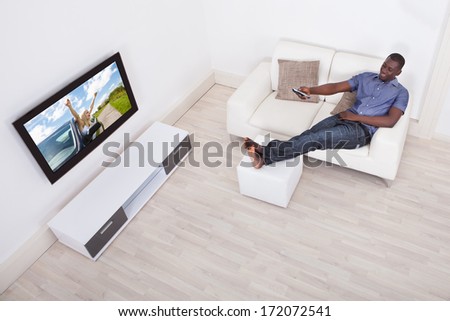 African Man Sitting On Sofa With Remote Holding In Hand