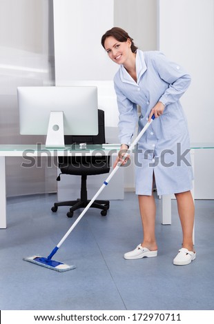 Portrait Of Happy Female Janitor Cleaning Floor At Office