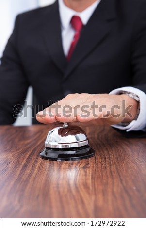 Close-up Of Hand Ringing Bell Kept On Wooden Table
