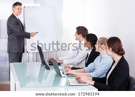 Mature Businessman Giving Presentation To His Colleagues At Office Meeting