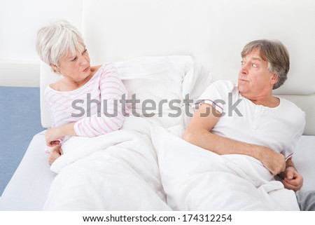 Angry Senior Couple Lying On Bed Looking At Each Other