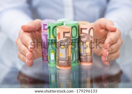 Close-up Of Hand Protecting Rolled Up Euro Banknote