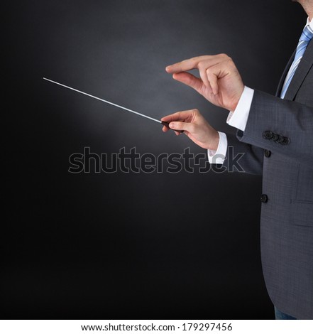 Close-up Of Orchestra Conductor Hands Holding Baton Over Black Background