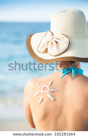 Rear view of young woman with sun drawn from sunscreen on back at beach
