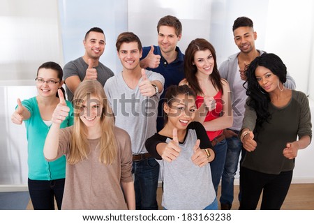 Group portrait of confident multiethnic university students gesturing thumbs up in classroom