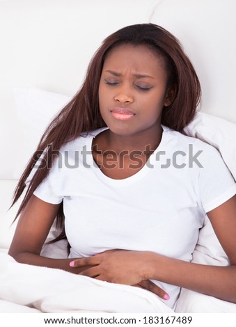 Young African American woman suffering from stomachache in bed at home