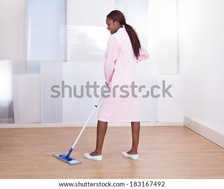 Full length of female housekeeper mopping floor in hotel