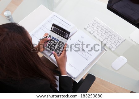 Portrait of confident businesswoman calculating tax at desk in office