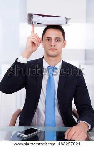 Portrait of young businessman balancing binder on head with index finger in office