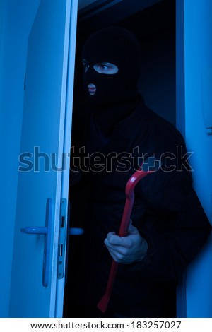 Thief holding crowbar while secretly entering into house