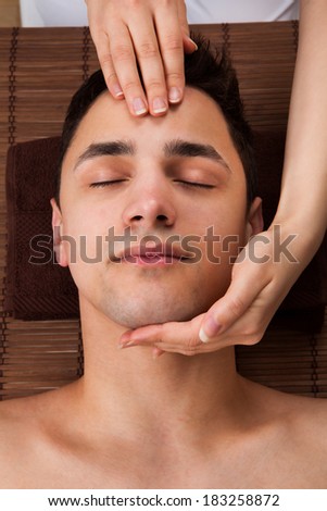 High angle view of young man receiving head massage from massager in spa