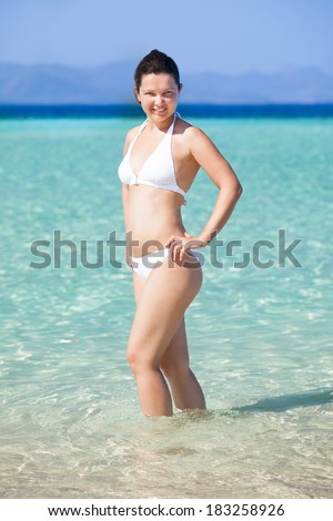 Portrait of happy young woman in bikini posing in sea at beach