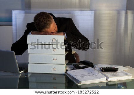 Exhausted businessman sleeping an a stack of files as he works late at the office during the evening as he tries to meet a deadline for the morning
