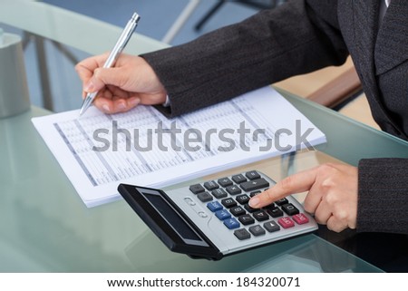 Midsection of businesswoman calculating tax at desk in office