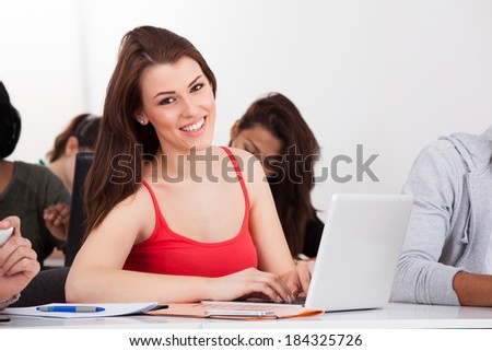 Portrait of beautiful university student sitting with laptop at desk in classroom