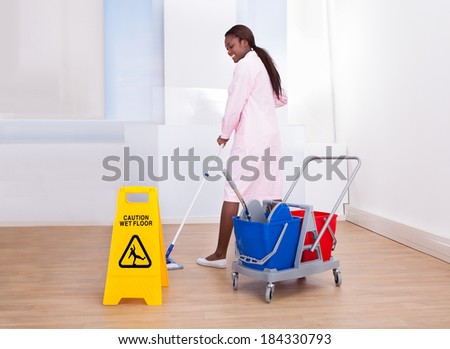 Full length of African American female housekeeper cleaning floor in hotel
