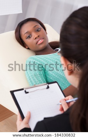 Happy female patient talking to psychologist while lying on bed in clinic