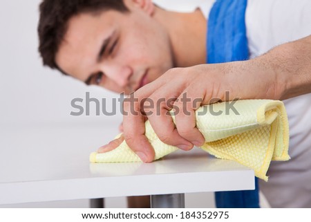 Handsome young man cleaning table with napkin at home