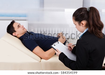Female psychologist writing notes while patient lying on bed in clinic