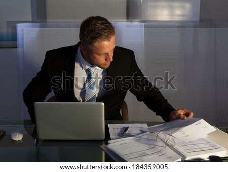 Businessman under pressure working overtime late into the evening sitting at his desk collating a report for a deadline in the morning