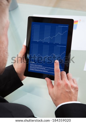 Businessman navigating on his tablet-pc using his finger on the touchscreen as he studies an online report  over the shoulder view of the screen