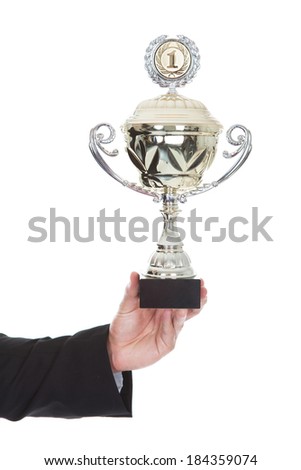 Hand of a businessman displaying a large silver trophy cup as a reward for his success and achievement isolated on white