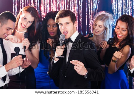 Portrait of handsome man singing into microphone with friends at karaoke party