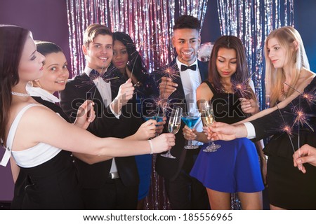 Happy multiethnic friends holding sparkling sticks while toasting drinks at nightclub