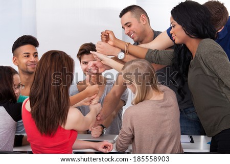 Group of university students piling fists at desk in classroom