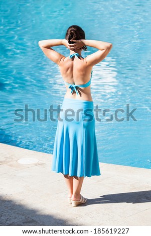 Full length rear view of woman with hands behind head standing at poolside