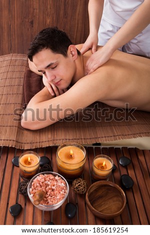 Relaxed young man with eyes closed receiving shoulder massage in spa