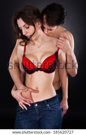 Passionate young man inserting hand in woman\'s jeans while kissing her on neck isolated over black background