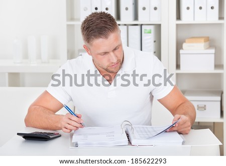 Businessman working at his desk in the office sitting writing notes in a short-sleeved white shirt