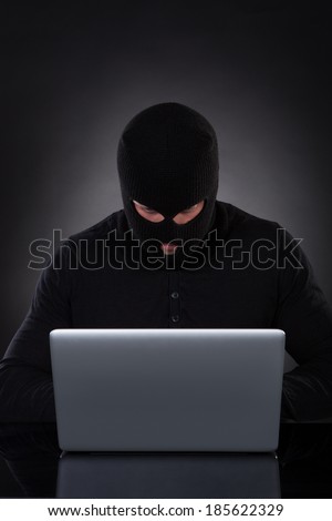 Man or hacker working on a laptop computer at night bending forwards over the keyboard in the glow from the screen as he browses the internet or retrieves and downloads personal data