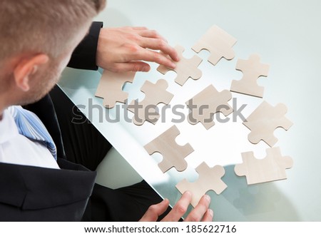 Businessman with a jigsaw puzzle spread out on his desk trying to match the pieces in a concept of problem solving and meeting business challenges  over the shoulder view from above