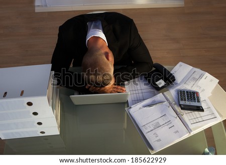 Exhausted businessman sleeping an a stack of files as he works late at the office during the evening as he tries to meet a deadline for the morning