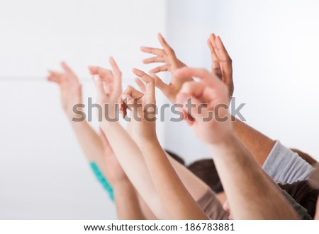 Row of multiethnic college students raising hands in classroom