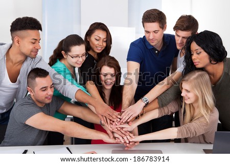 Group portrait of multiethnic university students stacking hands at desk in classroom