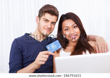 Portrait of smiling young couple with laptop and credit card shopping online at home