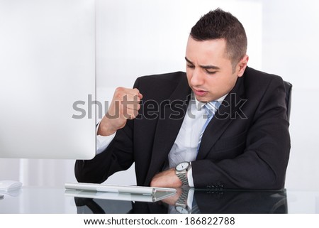 Stressed young businessman clenching fist at computer desk in office