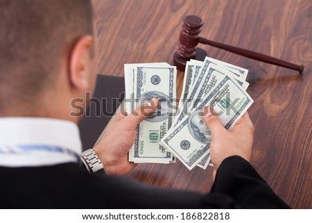 Rear view of male judge counting dollars in courtroom