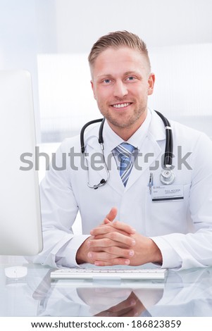 Smiling doctor or consultant sitting at a desk with his stethoscope around his neck looking at the camera