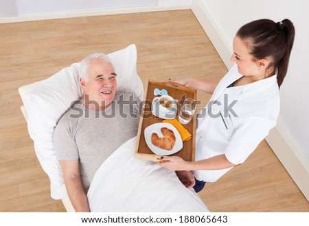 Young female doctor serving breakfast to senior man in hospital