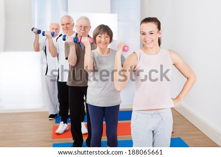 Portrait of happy trainer and senior customers exercising with dumbbells at gym