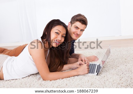 Side view of young couple using laptop together while lying on rug at home