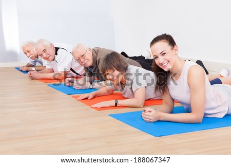 Portrait of smiling trainer and senior customers performing yoga on floor at gym