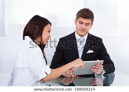Side view of female doctor showing digital tablet to businessman in clinic