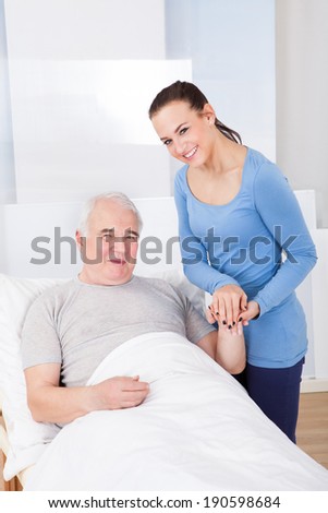 Portrait of happy young female caregiver with senior man in nursing home