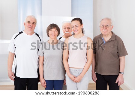 Full length portrait of confident trainer and senior customers standing together at healthclub