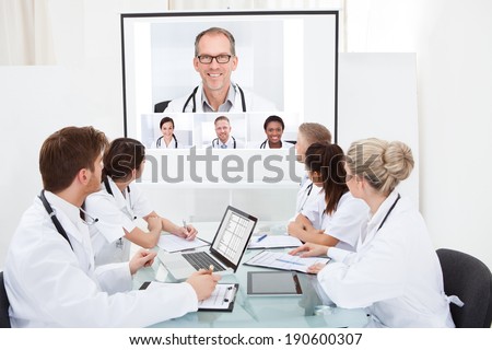 Team of doctors looking at projector screen in video conference meeting at hospital